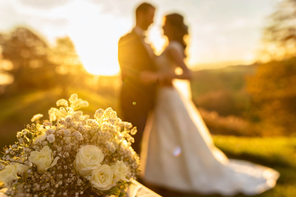 Tipps für Hochzeitsfotografie: Das Bild zeigt ein Hochzeitspaar mit starkem Gegenlicht und dem Brautstrauß im Vordergrund.